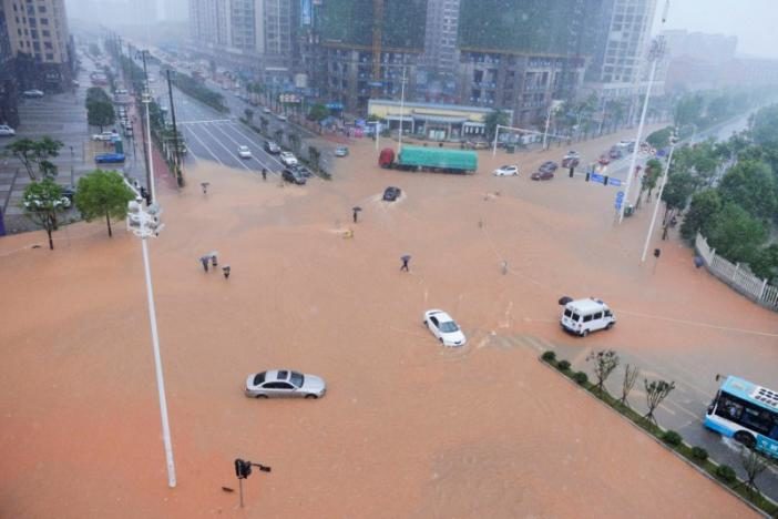 Pedestrians and vehicles cross a flooded street during heavy rain in Changsha, Hunan province, China, July 1, 2017.
