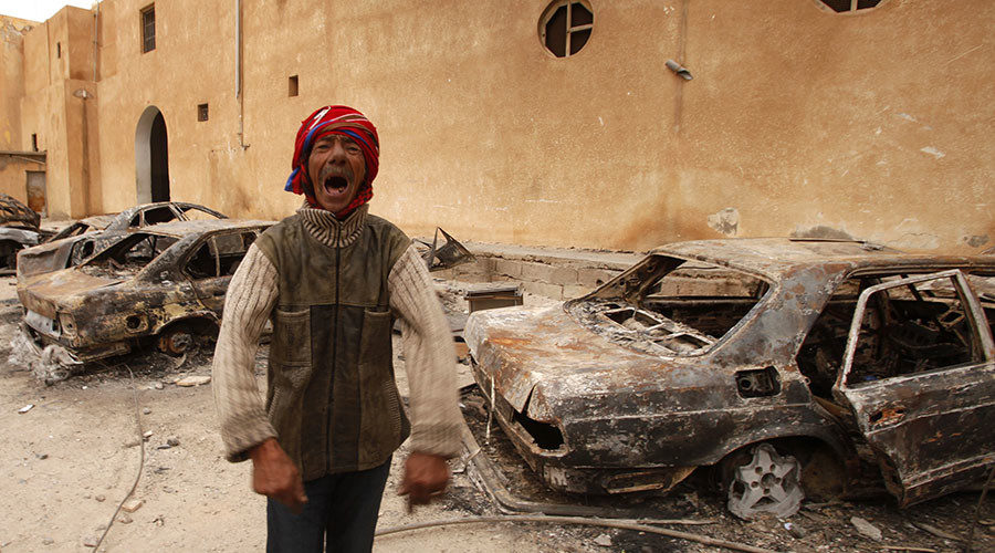 man gestures in front of burnt vehicles in a state security building in Tobruk
