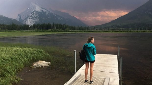 A woman takes in the smoke blanketing Mt. Rundle from a forest fire in Kootenay National Park as she stands on a dock on the Vermillion lakes near Banff, Alta. Sunday July 15, 2017.
