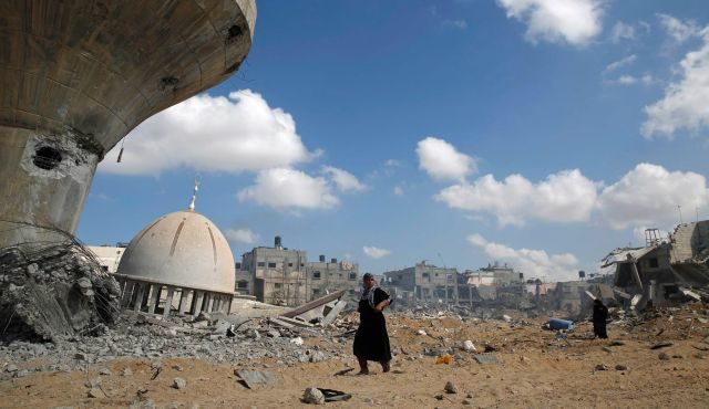 Palestinian women walk past a mosque and water tower damaged by Israeli air strikes