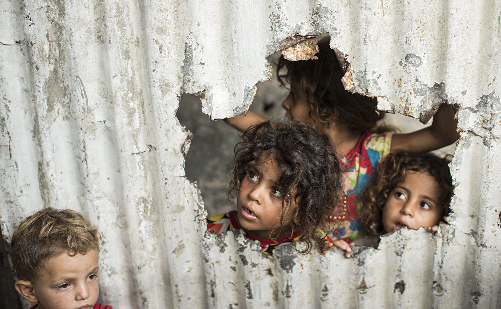 Palestinian children look through a hole in a sheet metal fence outside their home in a poor neighbourhood in Gaza City