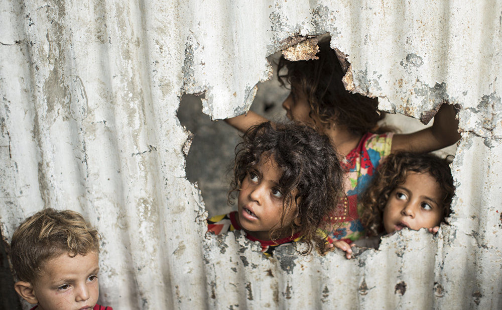 Click to enlarge Palestinian children look through a hole in a sheet metal fence outside their home in a poor neighbourhood in Gaza City