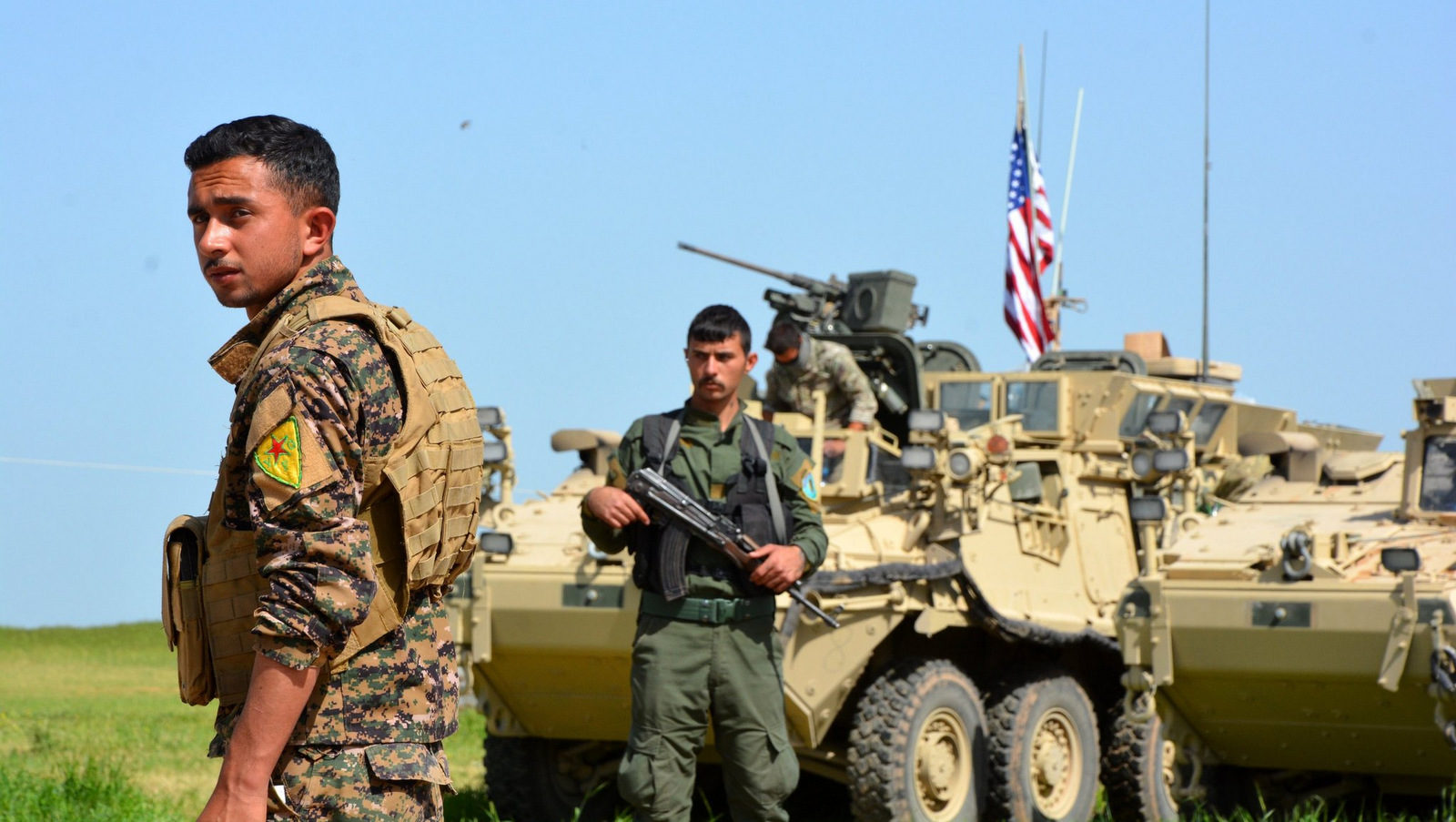 Kurdish fighters from the People’s Protection Units, (Y.P.G), stand guard next to American armored vehicles at the Syria-Turkey border