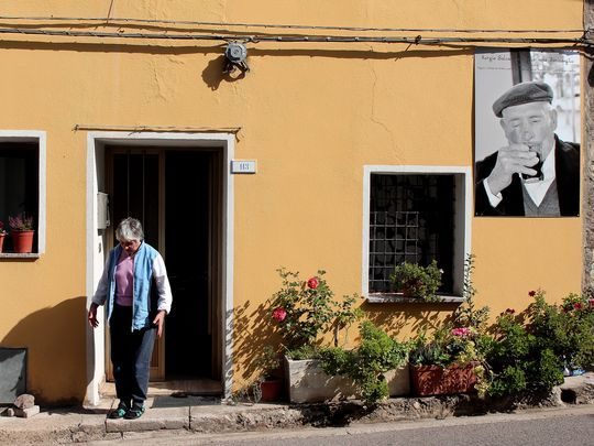 A resident of Seulo, Italy, leaves a home that is adorned with a black-and-white photo of a centenarian who previously lived there.