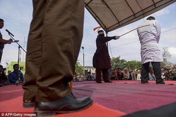 Click to enlarge An Islamic enforcer holds the rattan stick against the back of Simbolon, who was whipped 36 times for selling alcohol in the province