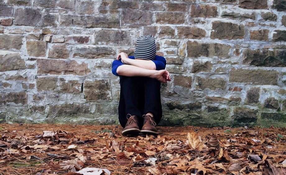 Stock photo of a teen sitting against a stone wall.