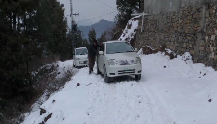 Click to enlarge A man pushes a car up a snowy slope.