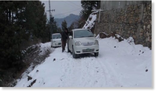 A man pushes a car up a snowy slope.