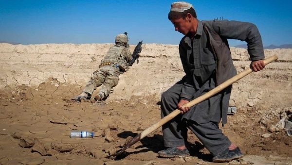 An Afghan boy works at a construction site behind a US Army soldier in Logar province, Afghanistan.