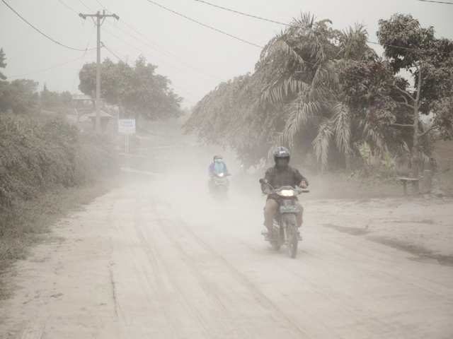 Motorists ride on a road covered in volcanic ash