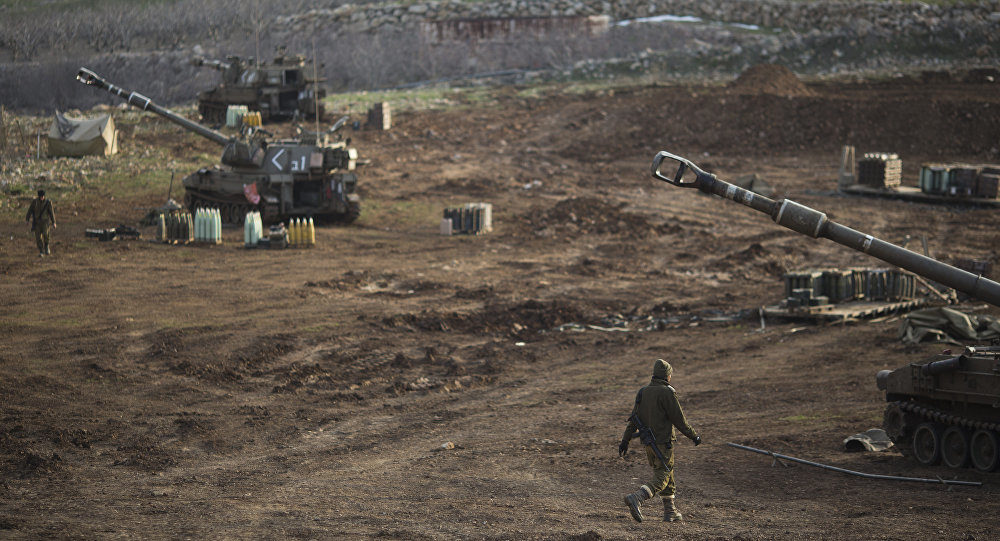 Israeli soldiers walk next to mobile artillery units