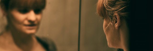 Sad and lonely woman looking at her reflection in the mirror