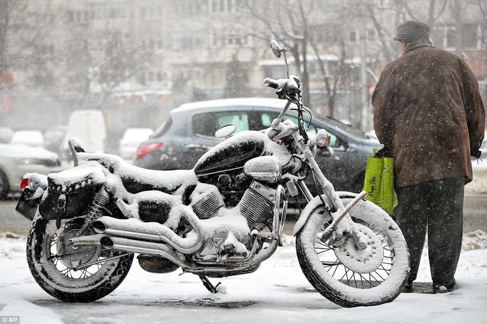 A man stands next to a snow covered motorcycle in Bucharest, Romania, where the city has been pelted with cold conditions