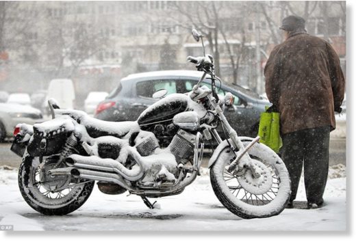 A man stands next to a snow covered motorcycle in Bucharest, Romania, where the city has been pelted with cold conditions