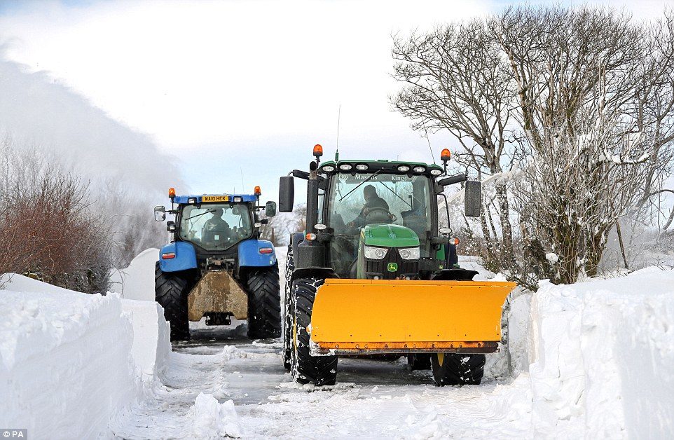 Farmers in their tractors help to clear the snow from a blocked road on Exmoor, Somerset