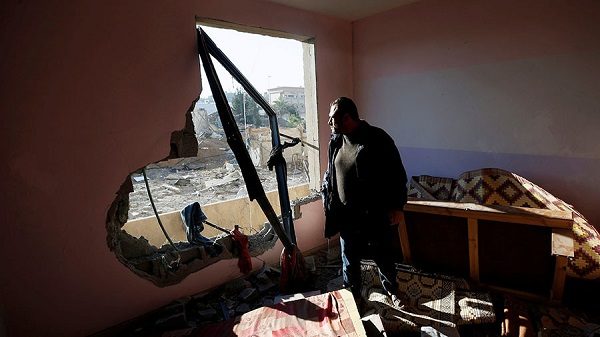 A Palestinian man looks out of his  damaged apartment