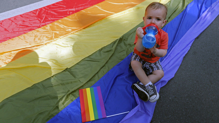A baby sits on an LGBT flag.