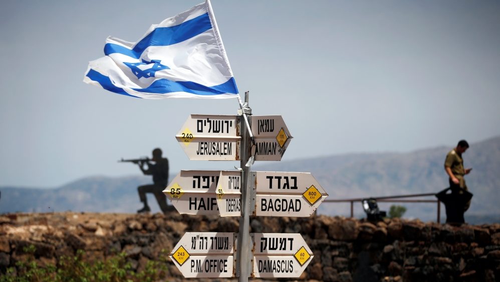 An Israeli soldier stands next to signs showing distances to different cities