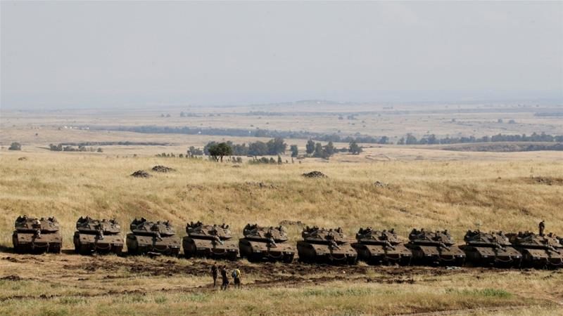 Israeli soldiers walk past tanks