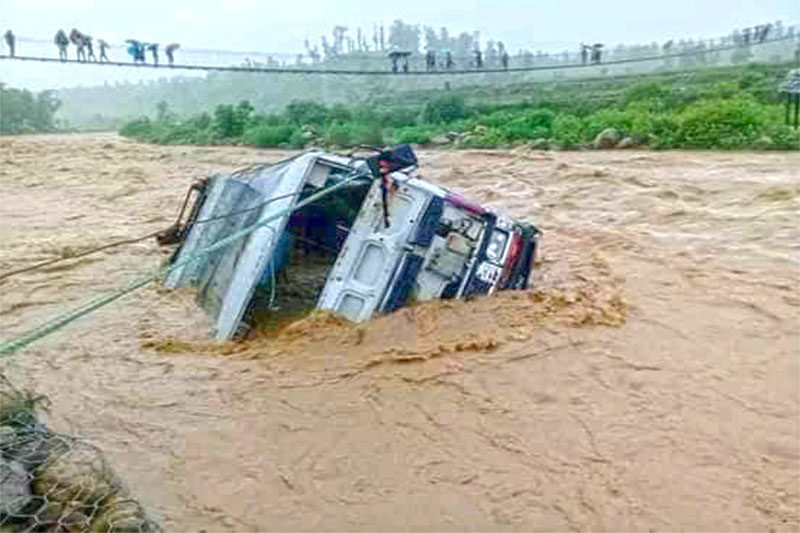 A passenger bus swept by flood lies roped as locals look from a suspension bridge at Tawang River in Western Dang. No human casualties were reported in the incident.