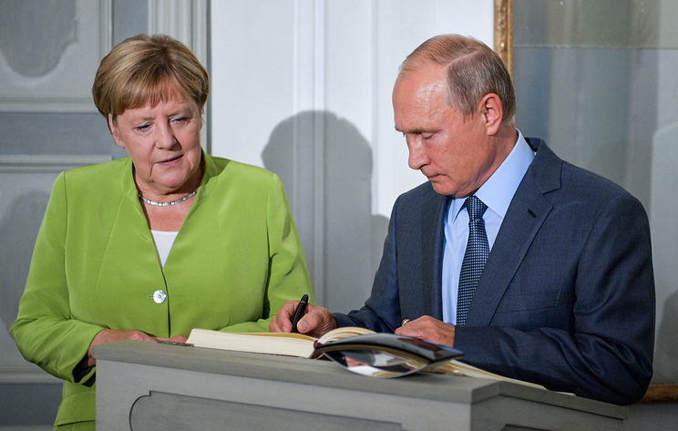 Russia's President Vladimir Putin signs a distinguished visitors' book as he meets with German Chancellor Angela Merkel