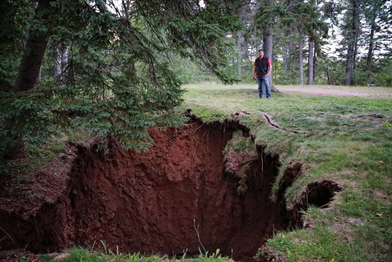 Click to enlarge Mark Rushton stands near a large sinkhole that developed in the Oxford Lions Park.