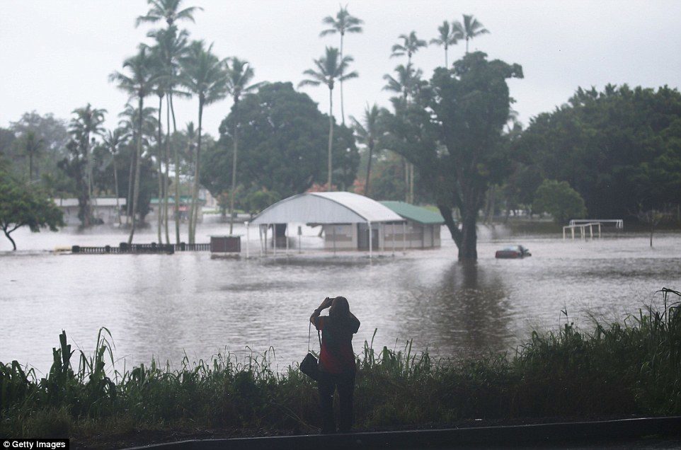 Pictured is a woman taking photos of floodwaters from Lane on the Big Island on Thursday