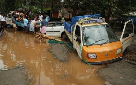 Indian people look at vehicles stuck in the mud along a flooded road at Kannappankundu in Kozhikode, in the Indian state of Kerala on 10 August 2018.