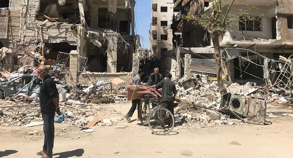 People stand in front of damaged buildings