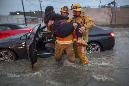 A firefighter carries a woman from her car after it was caught in street flooding in Sun Valley, California