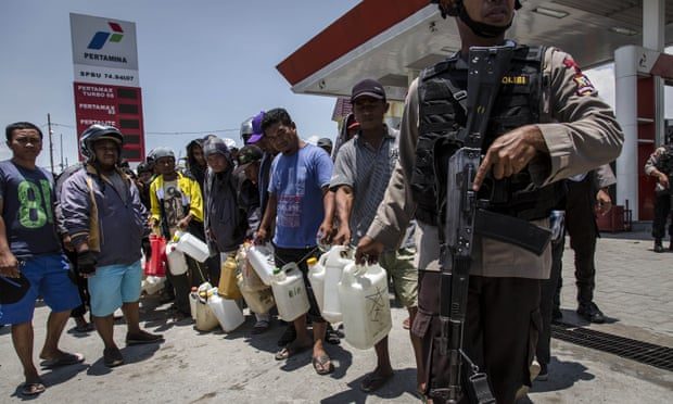 Click to enlarge Indonesian police guard a petrol station as people queue for fuel in Palu.