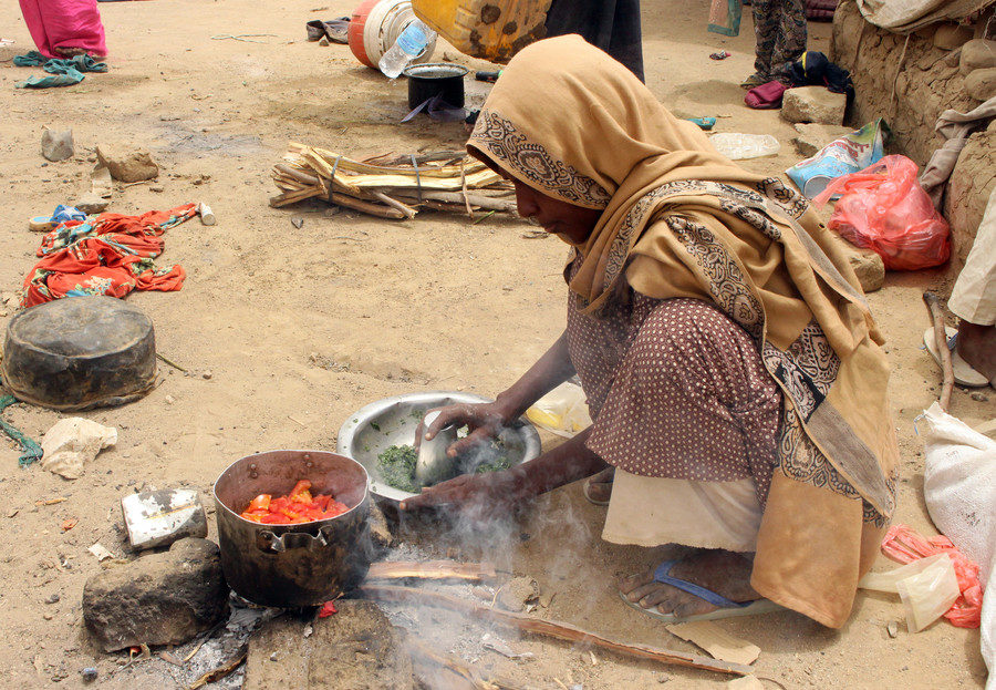 Click to enlarge A displaced Yemeni woman from Hodeida cooks food outside a shelter