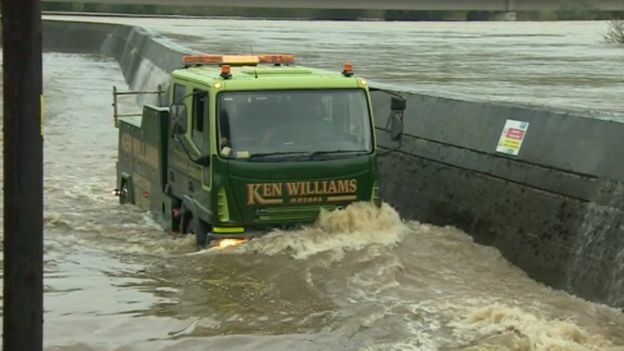 A van drives through the flood water as the River Towy defences at Carmarthen are breached