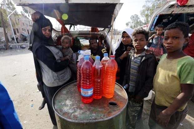 Click to enlarge Yemenis stand near bottles full of fuel displayed for sale at a black market, amid an acute shortage of fuel in Sana’a