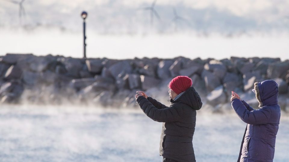People take pictures as mist rises from Lake Ontaro