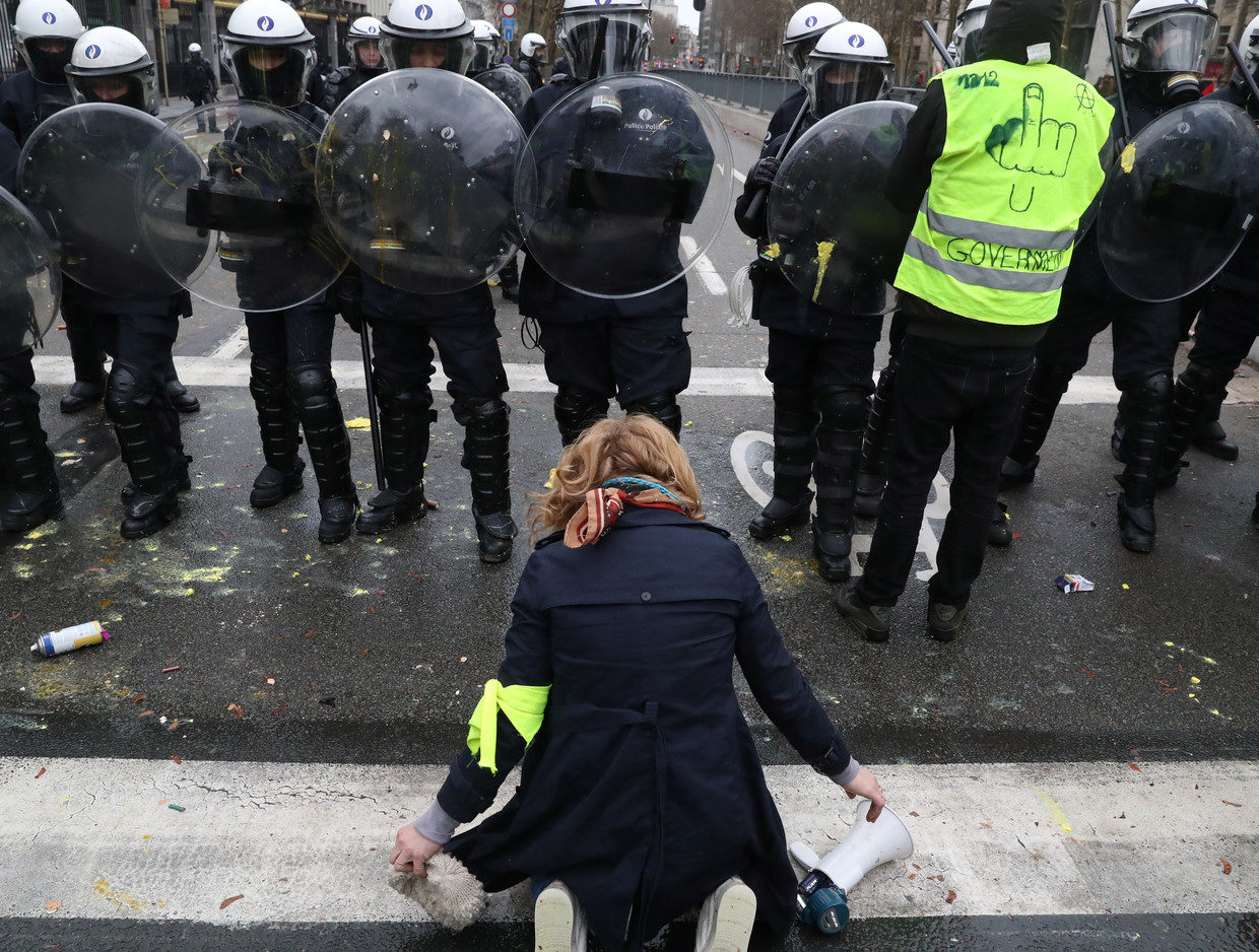 A woman kneels in front of police blocking the street during the 