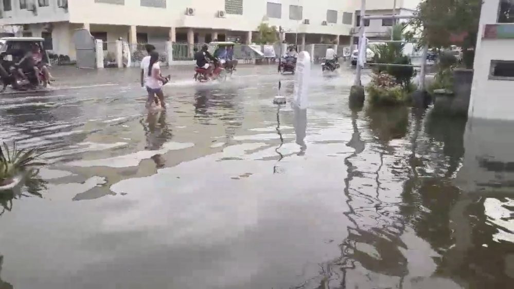 Click to enlarge Pedestrians and vehicles move along a flooded