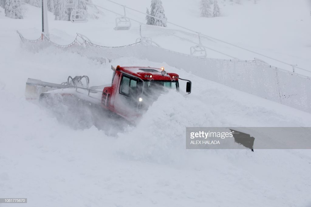 A snowcat drives through the snow at the valley