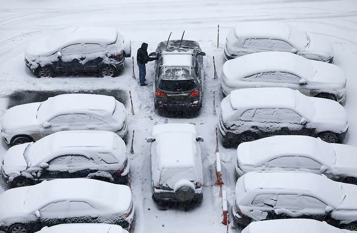 A man clears snow off his car during a snowfall in Moscow