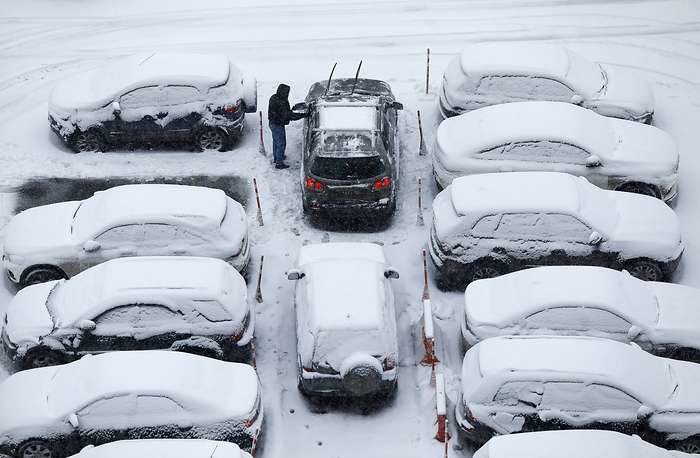 Click to enlarge A man clears snow off his car during a snowfall in Moscow