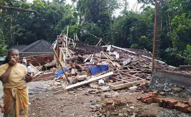 A resident of Montong Gading district, East Lombok, stands by her collapsed house after an earthquake on Sunday