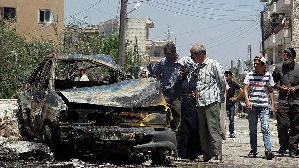 Civilians inspect a burnt car at a site hit by an airstrike in the rebel-controlled city of Idlib, Syria June 29, 2016
