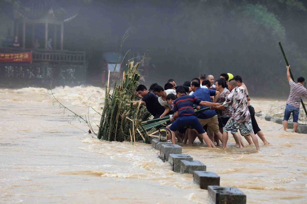 Disaster relief personnel and villagers work together to remove debris stuck near a bridge amid flooding in Liuzhou