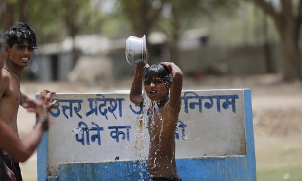 Indian boys bath at a drinking water tap on a hot day in Prayagraj, India