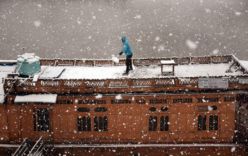 A boatman clears snow from his boat during the first snowfall in Srinagar