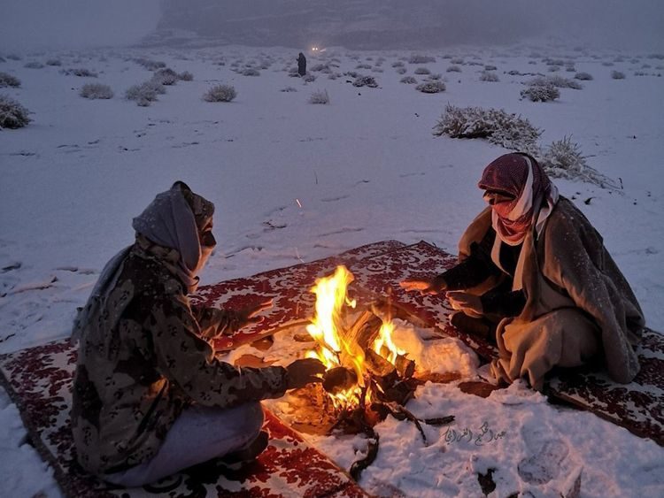 Two men camp out by a fire in Tabuk during the snow.