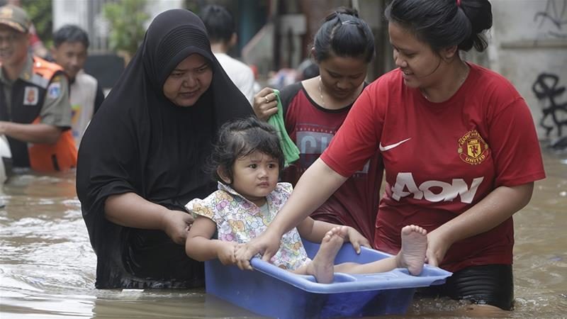 Residents carry a young girl as they walk in a flooded street in Jakarta, Indonesia