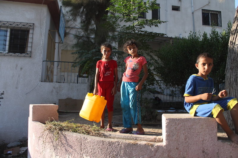 Palestinians displaced by Israeli airstrikes wait to get water from portable tanks
