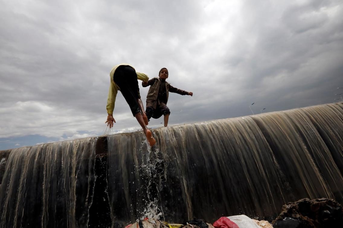 Click to enlarge A Yemeni child helps his friend to cross a flooded stream of rainwater following heavy rains in Sana'a, Yemen.