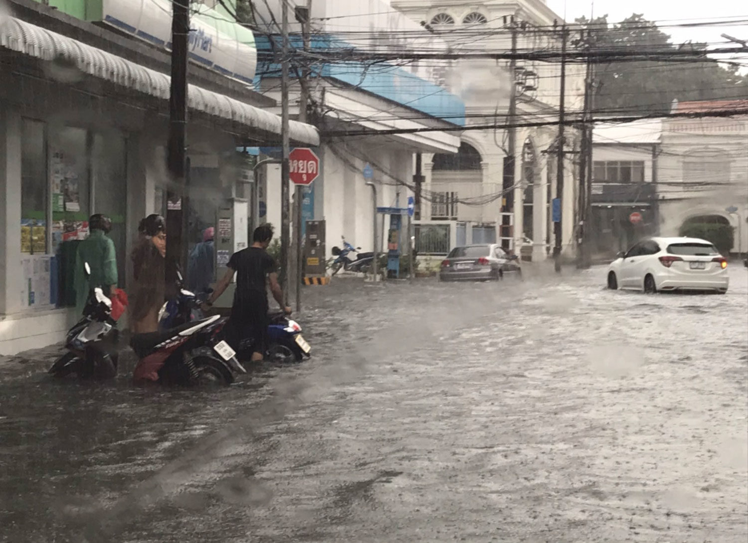 Motorcyclists take refuge in front of a convenience store on a flooded road.